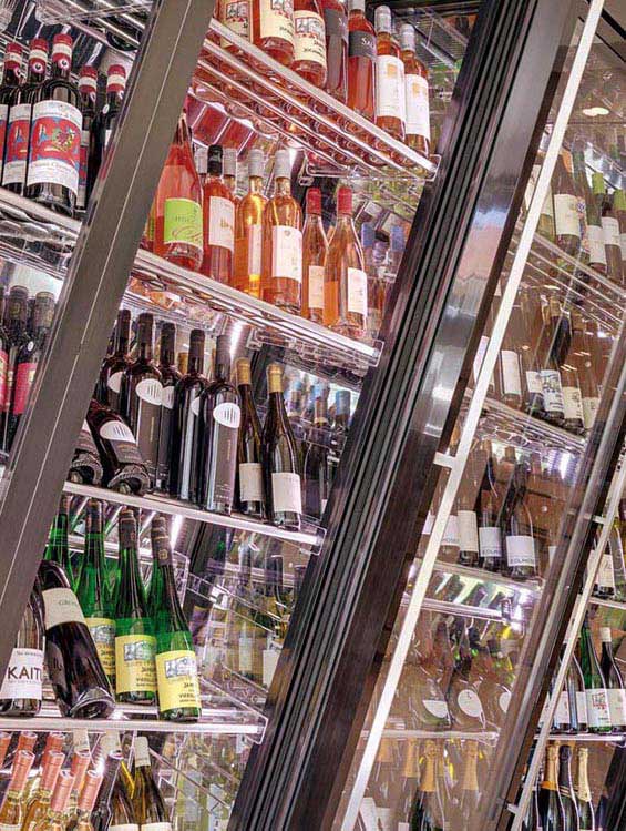 Eleganter Weinkühlschrank mit schräg angeordneten Glasregalen, gefüllt mit einer Vielzahl von Weinflaschen in verschiedenen Farben und Sorten. Die reflektierende Glasfront verstärkt den luxuriösen Eindruck.